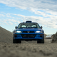 front-end view of a blue subaru coupe parked among piles of gravel in an industrial lot